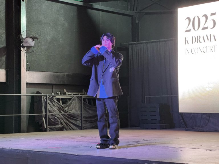 foto do dia em que o KISU fez o coquetel de lançamento da turnê. é ele no palco fazendo um coração com as mãos