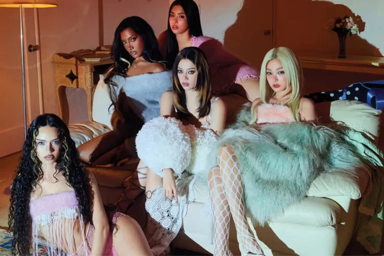 As cinco integrantes do KATSEYE posam juntas em uma sala, usando looks em tons de rosa, branco, cinza e preto, em imagem promocional relacionada ao filme KATSEYE: Wild Hearts.