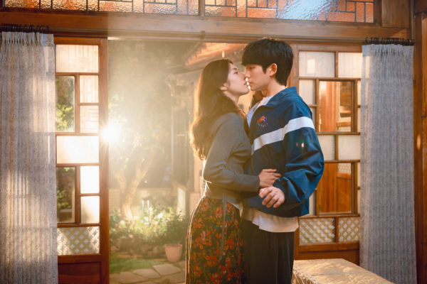 O ator coreano Jung Hae-in e a atriz coreana Ha Young se aproximam para um beijo em cena romântica do K-drama Um Grude de Amor, da Netflix, dentro de uma casa iluminada pela luz do sol.